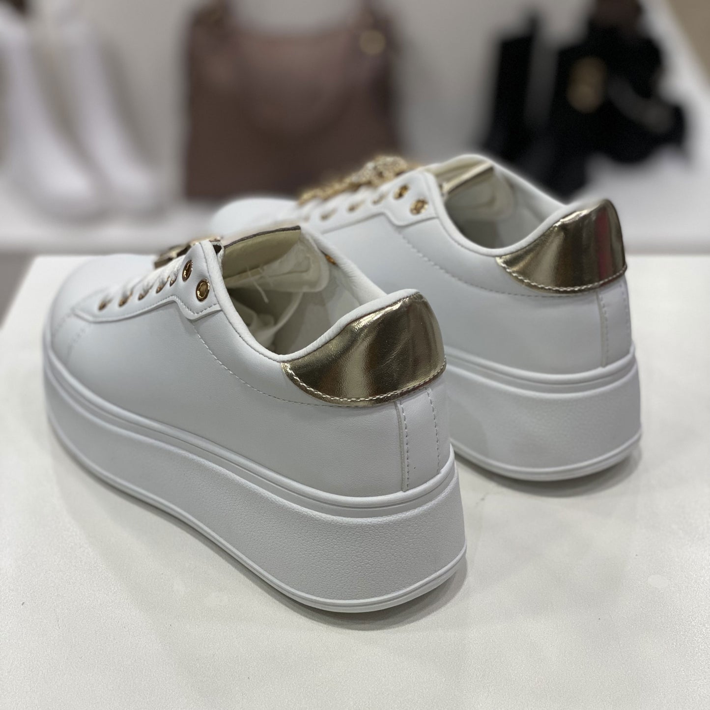 Un paio di scarpe da ginnastica bianche con dettagli metallici dorati sul retro. La suola alta e piatta conferisce un aspetto moderno e di tendenza, perfetto per un look casual ma ricercato.