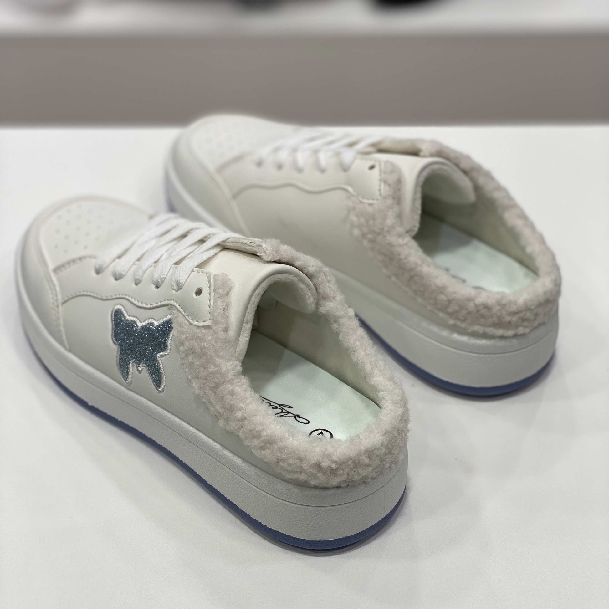 Parte posteriore di sneakers a ciabatta bianche con interno peluche e suola bianca, vista del tallone su sfondo neutro