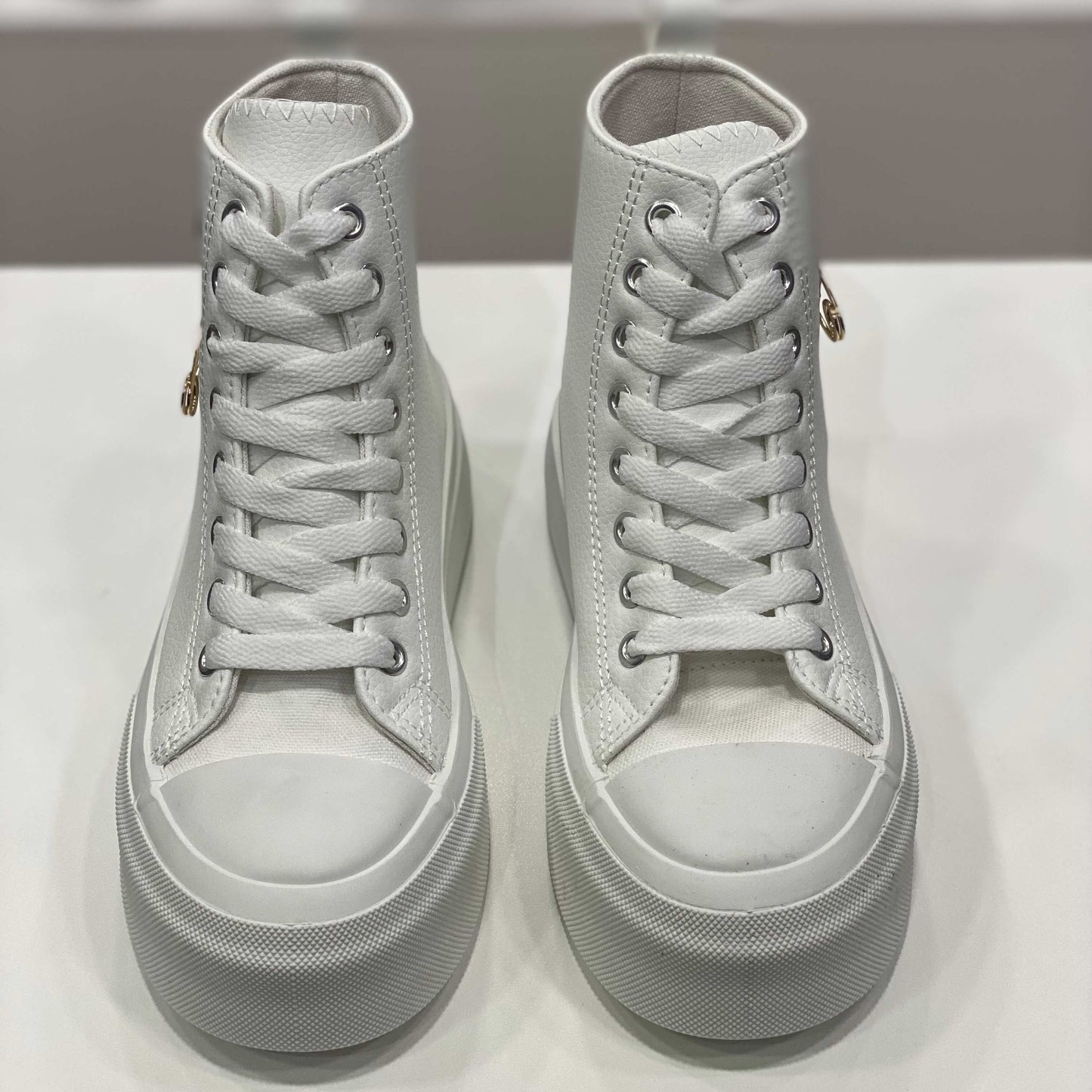 Sneakers alte bianche con spilla dorata applicata, vista frontale per evidenziare il design selvaggio e originale