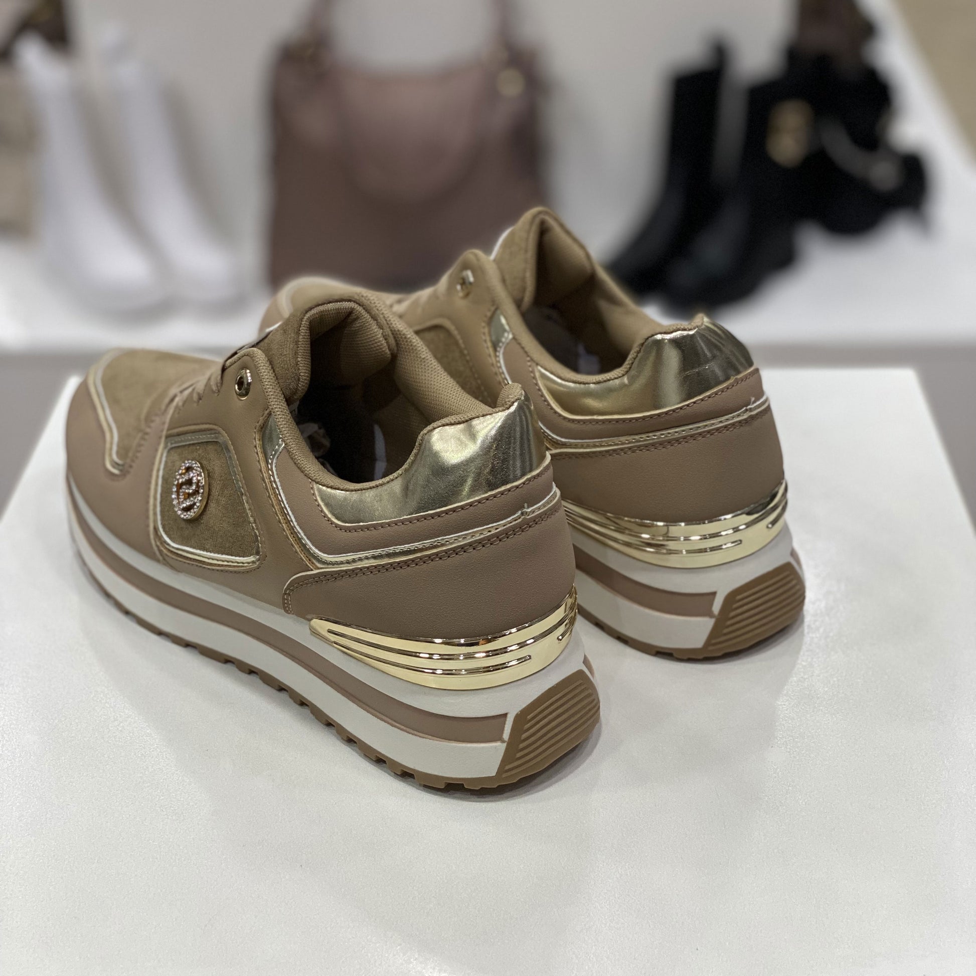 Parte posteriore di sneakers beige con dettagli metallici dorati, vista del tallone su sfondo neutro