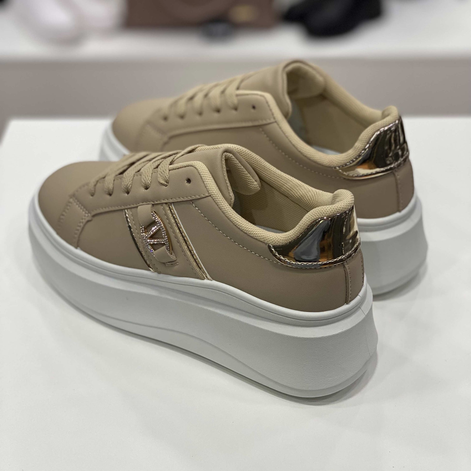 Parte posteriore di sneakers beige con dettaglio dorato sul tallone, vista del tallone su sfondo neutro
