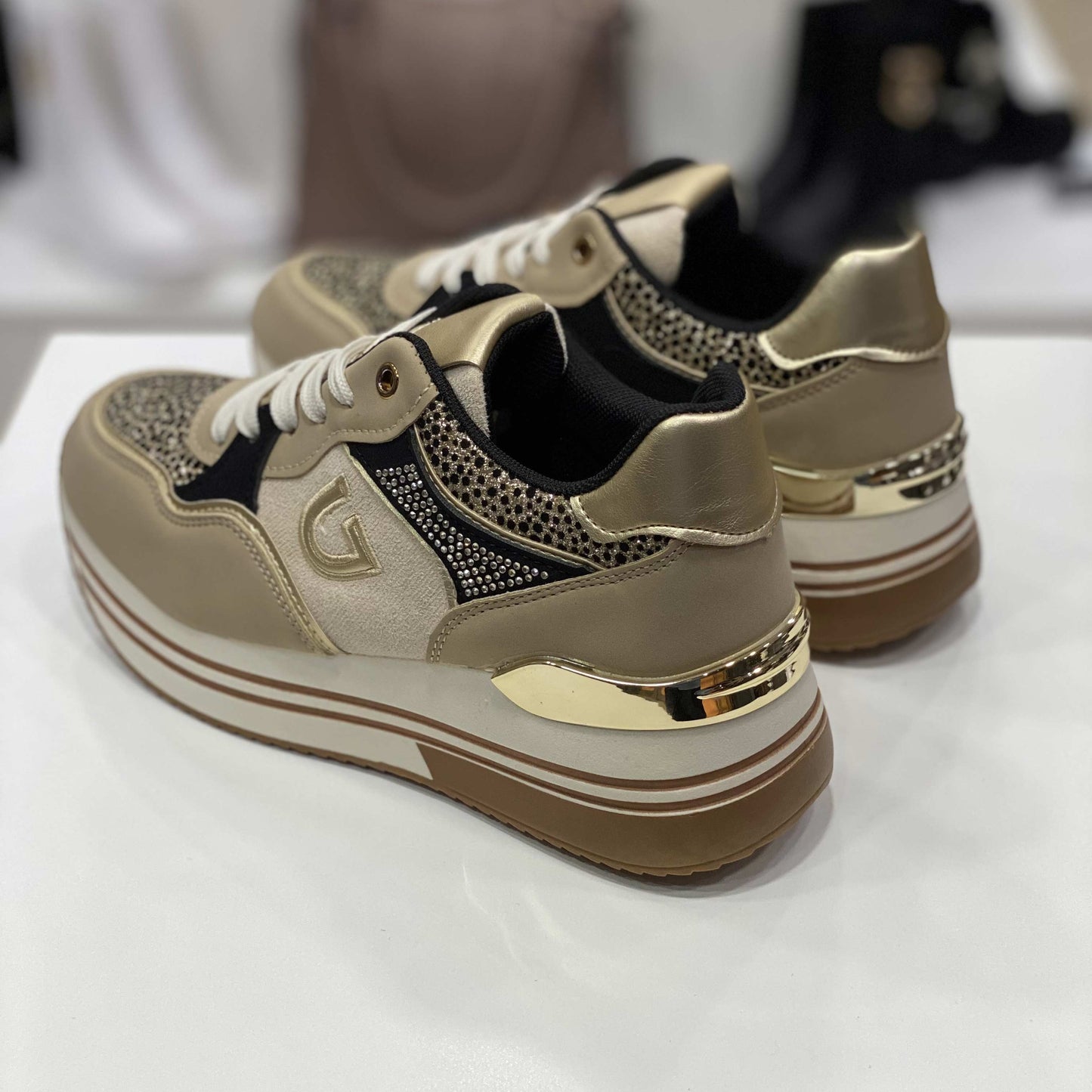 Parte posteriore di sneakers beige con tallone dorato e decorazioni glitter, vista del tallone su sfondo neutro