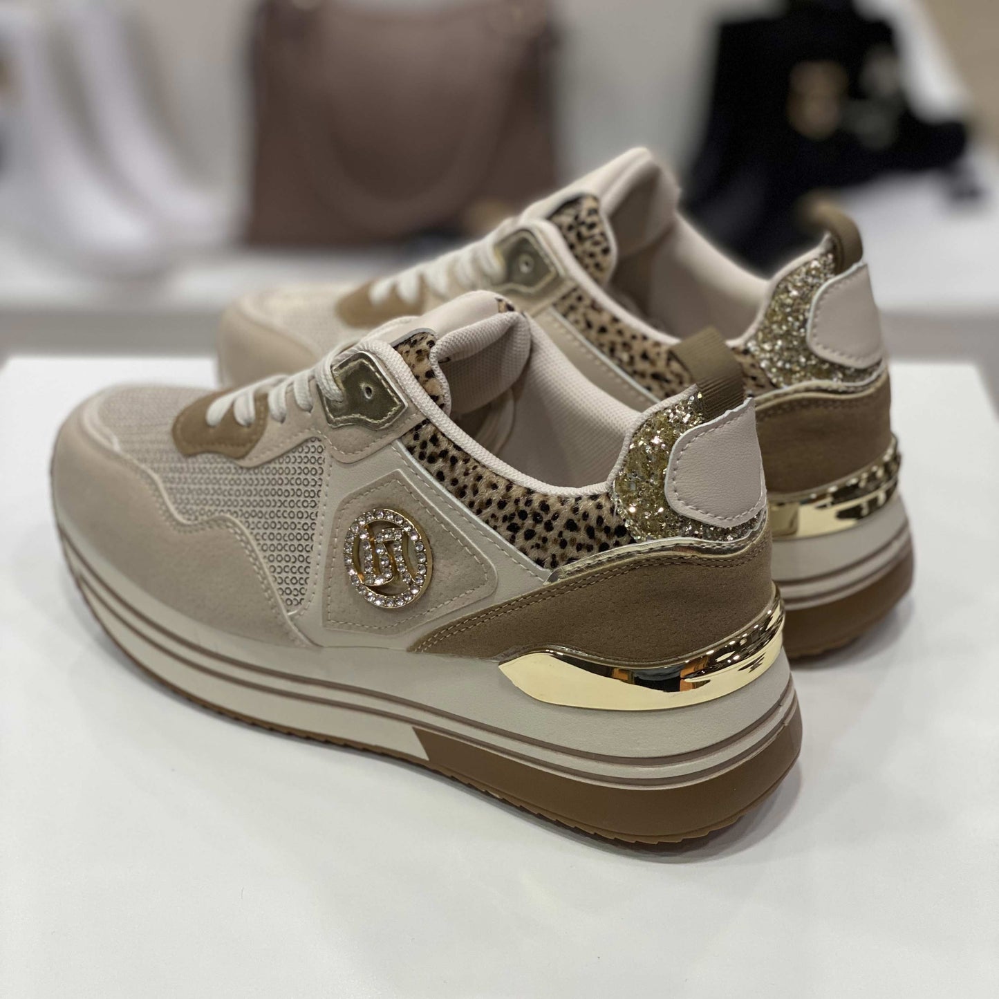 Parte posteriore di sneakers beige con glitter dorati e tallone decorato, vista su sfondo neutro