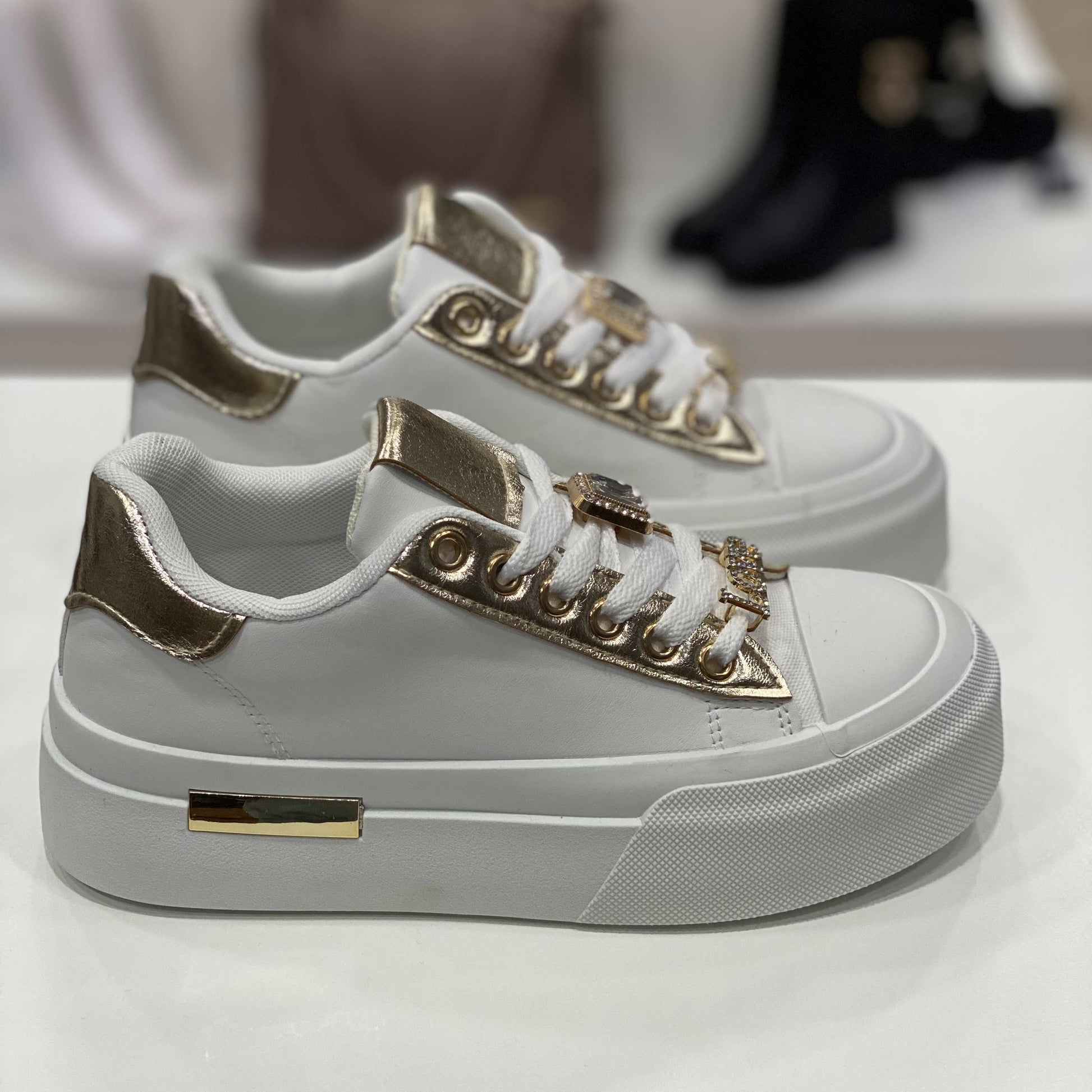 Sneakers bianca con dettagli dorati sui lacci e sul tallone, decorazioni gioiello e suola alta bianca, vista laterale