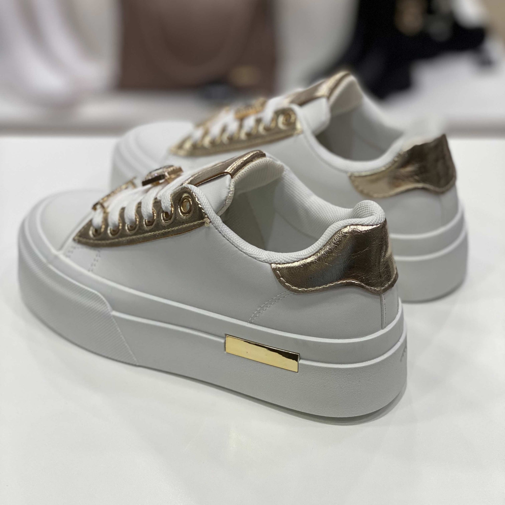 Parte posteriore di sneakers bianca con tallone dorato lucido e suola alta bianca, vista del tallone su sfondo neutro