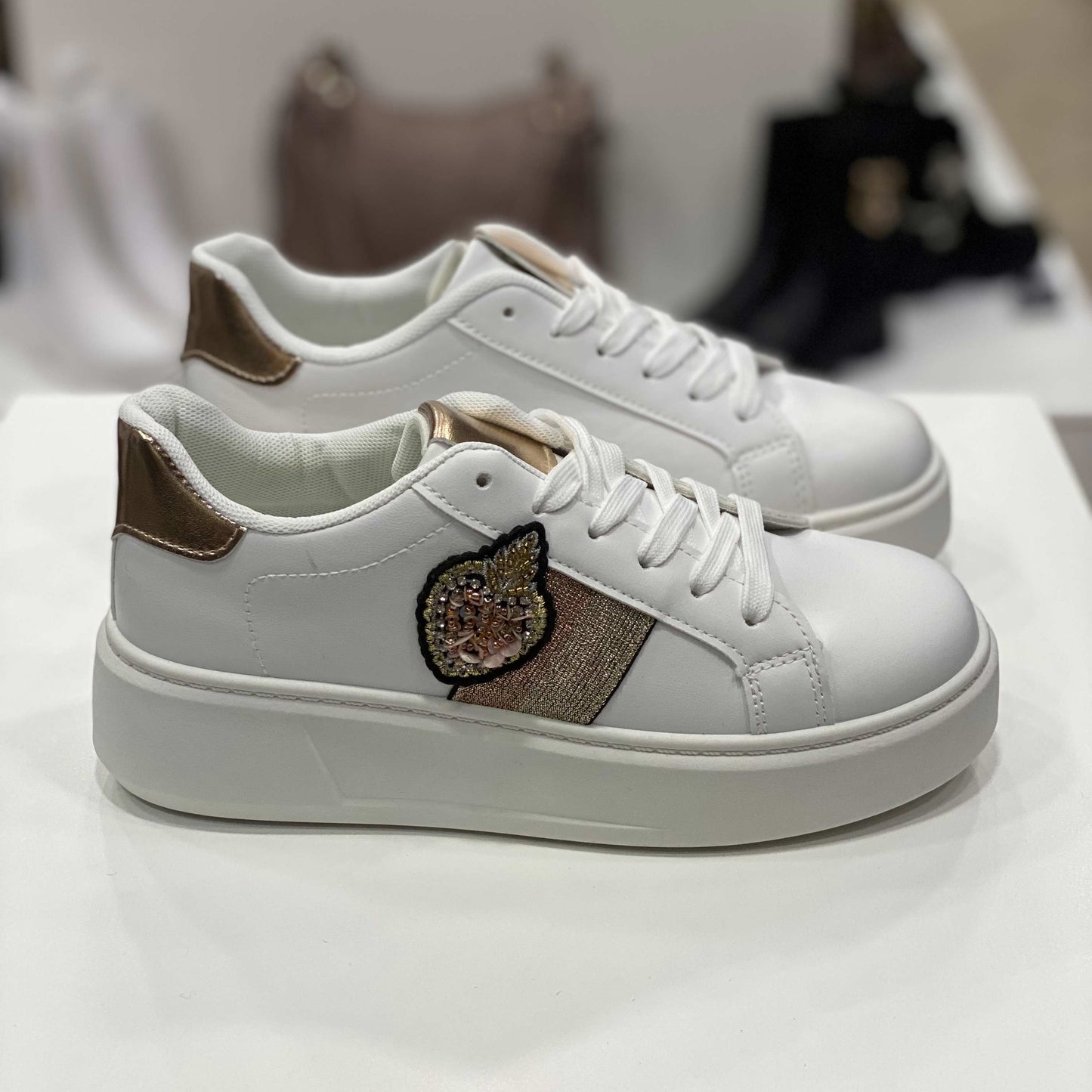 Sneakers bianche con applicazione gioiello a forma di frutto e dettagli dorati sul tallone e fascia laterale, vista laterale su sfondo neutro