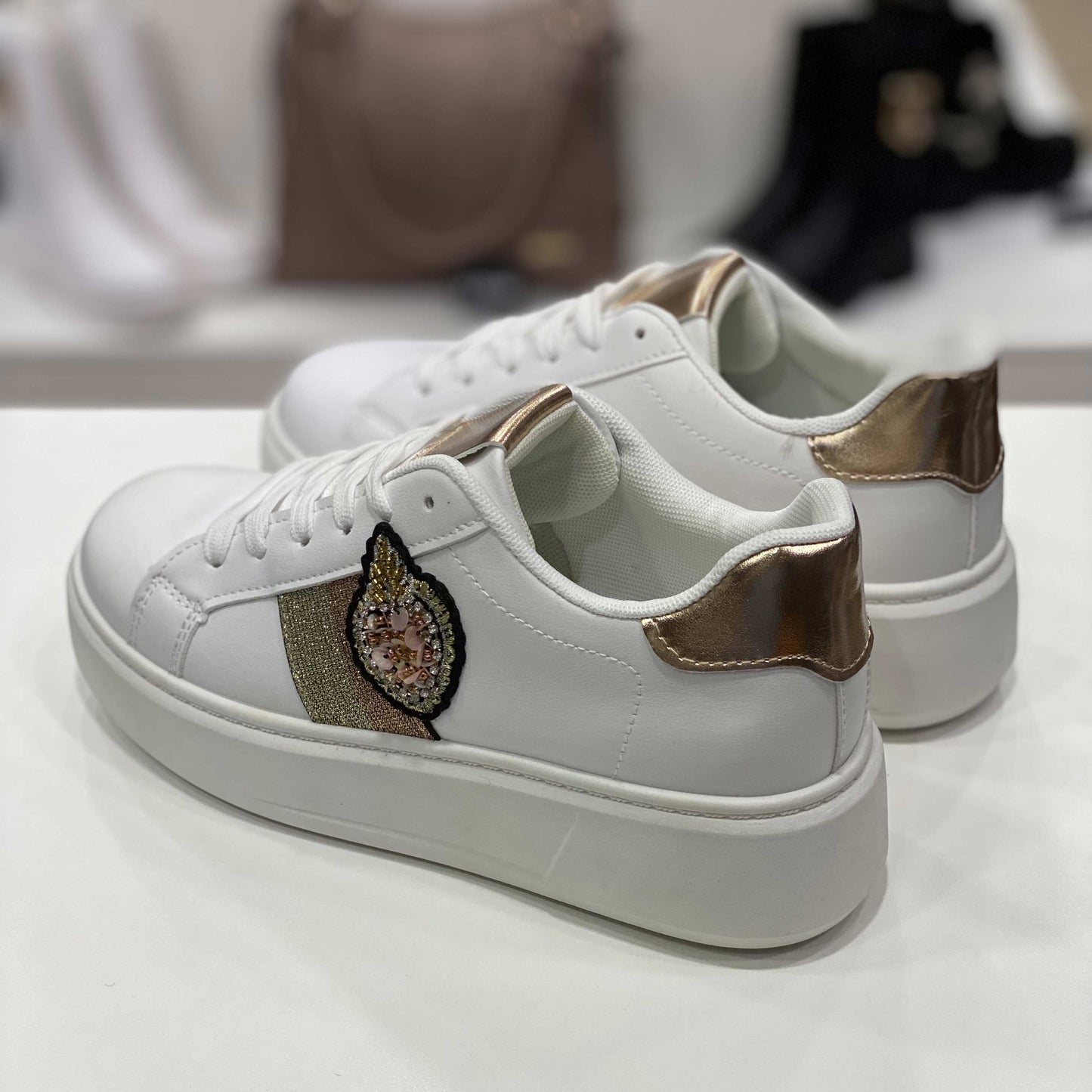 Parte posteriore di sneakers bianche con tallone dorato e applicazione gioiello, vista del tallone su sfondo neutro