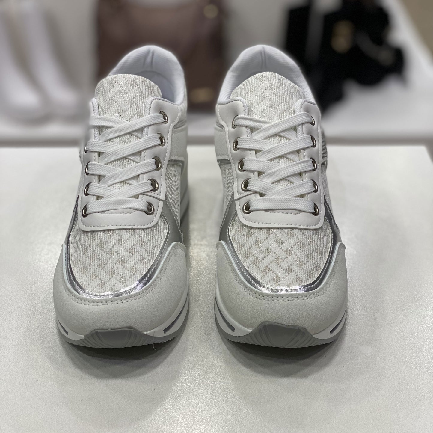 Sneakers bianche con dettagli metallici argentati, vista frontale su sfondo neutro