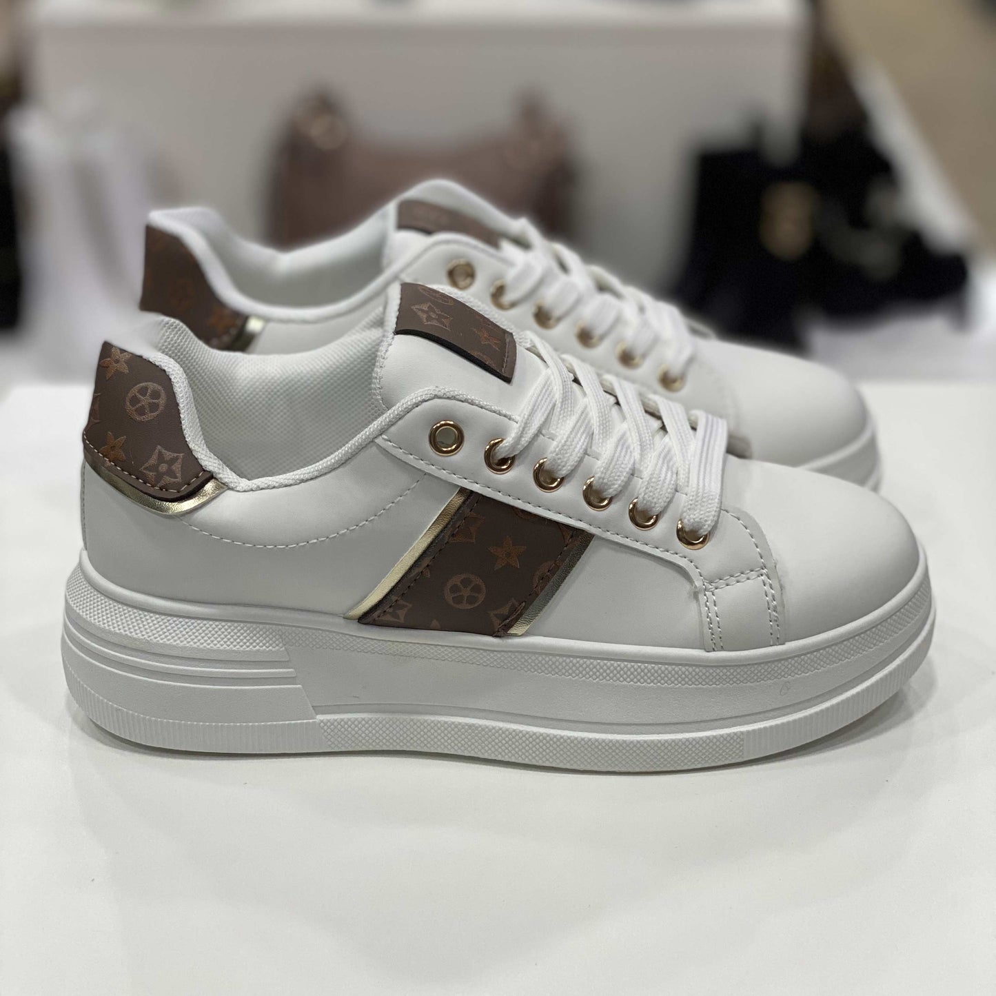 Sneakers bianche con dettagli monogram marroni e suola bianca, vista laterale su sfondo neutro