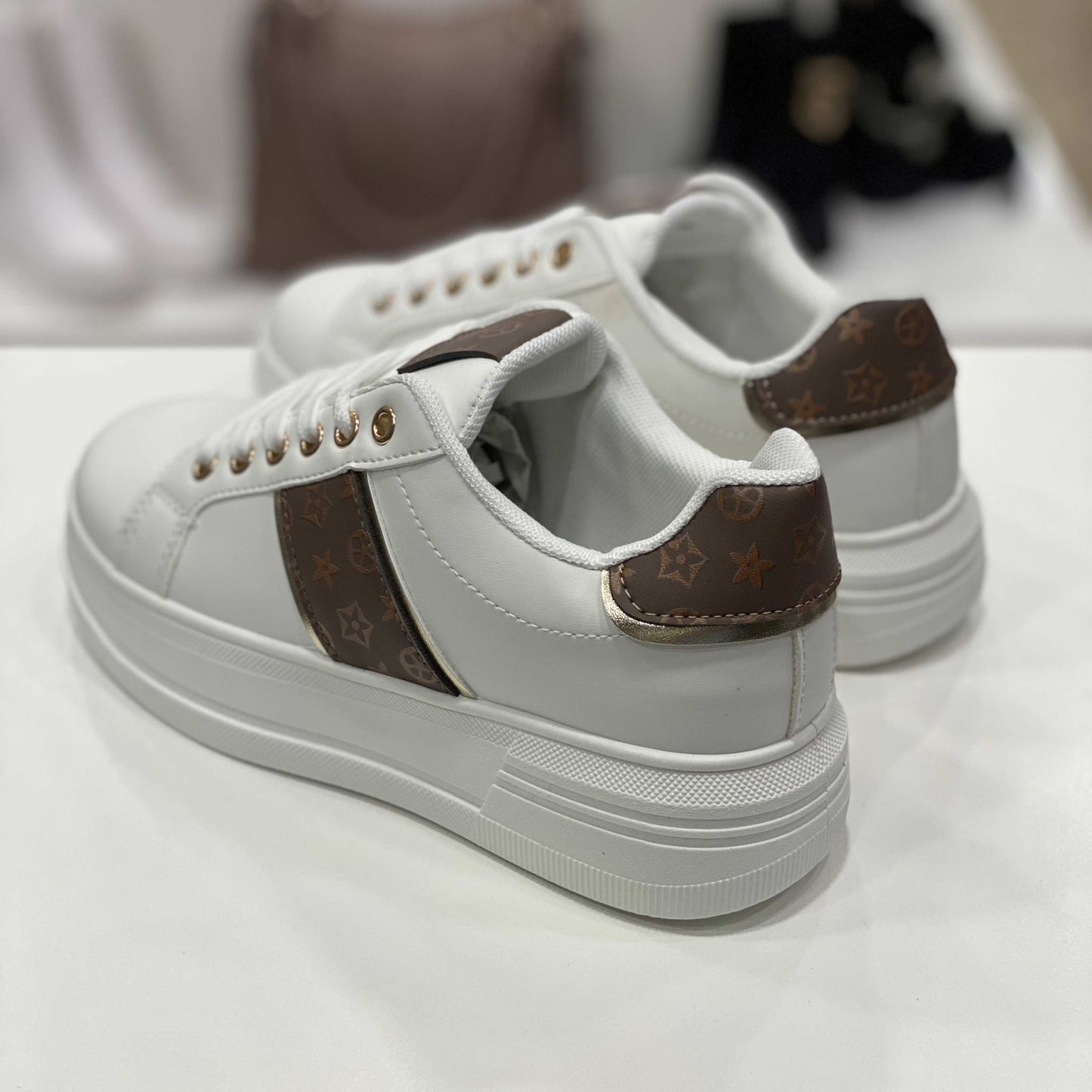 Parte posteriore di sneakers bianche con dettagli monogram marroni, vista del tallone su sfondo neutro