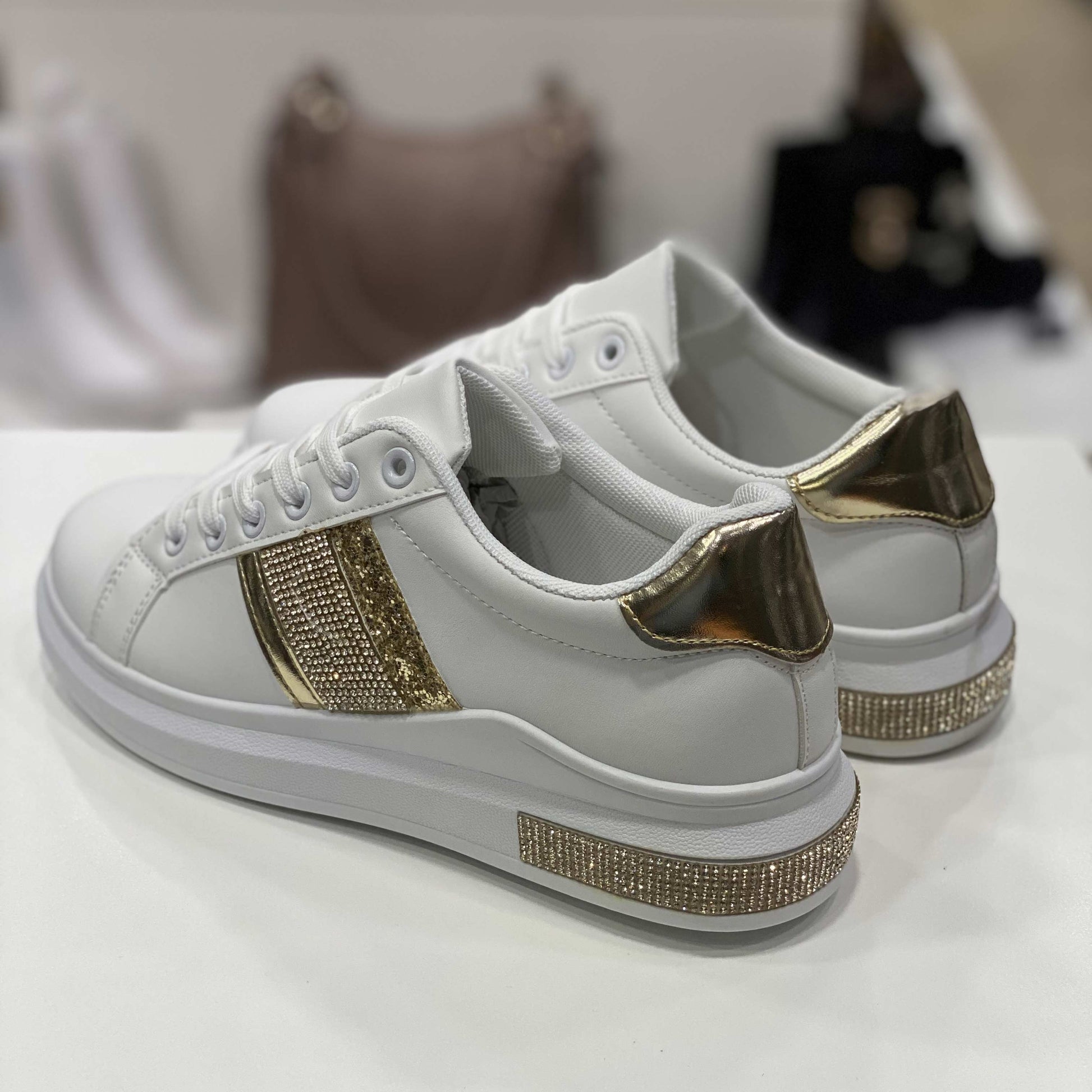 Parte posteriore di sneakers bianche con tallone dorato e decorazioni glitterate, vista del tallone su sfondo neutro