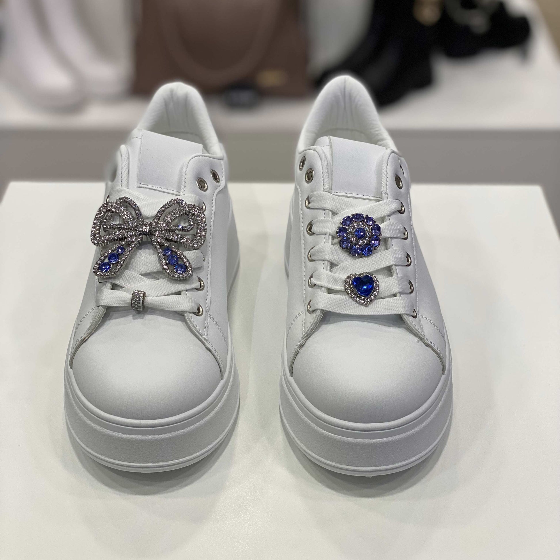 Sneakers bianche con fiocco gioiello e dettaglio argento sul tallone, vista frontale su sfondo neutro