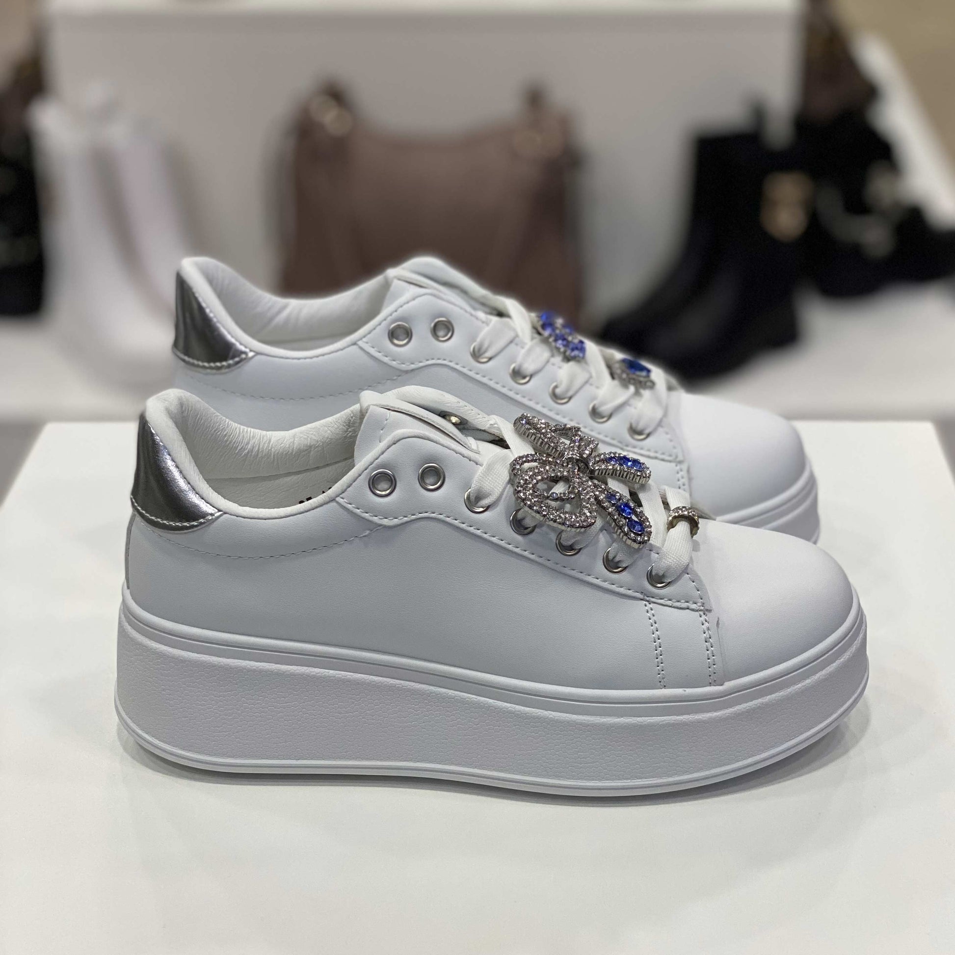 Sneakers bianche con gioiello a forma di fiocco e dettaglio argento sul tallone, vista laterale per mostrare il design e gli ornamenti