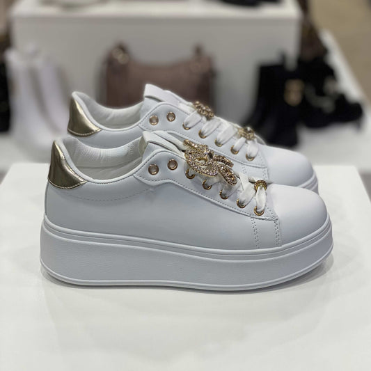 Sneakers bianche con gioiello a forma di fiocco e dettaglio oro sul tallone, vista laterale per mostrare il design e gli ornamenti
