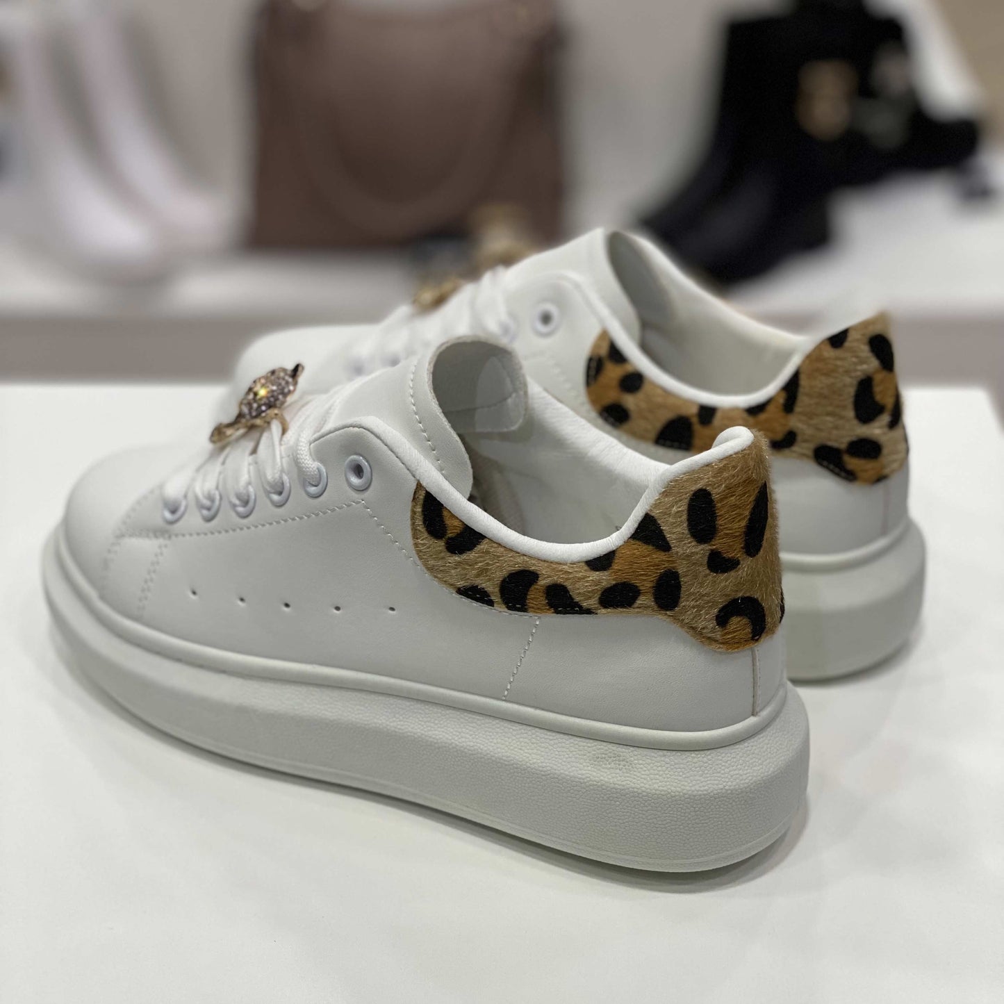 Parte posteriore di sneakers bianche con tallone leopardato e suola alta, vista del tallone su sfondo neutro