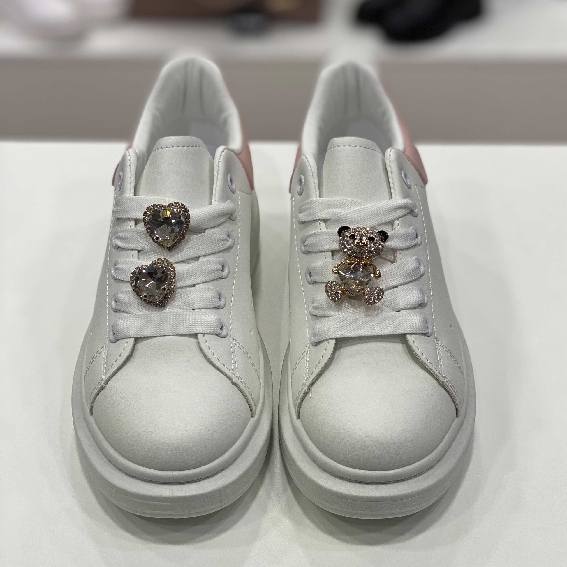 Sneakers bianche con gioielli decorativi e tallone rosa pastello, vista frontale per evidenziare i dettagli eleganti