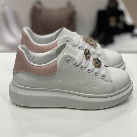 Sneakers bianche con decorazioni gioiello sui lacci e tallone rosa pastello, vista laterale su sfondo neutro