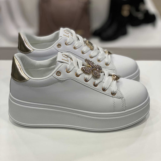 Sneakers bianche con decorazione gioiello a forma di farfalla e dettagli oro lucidi sul tallone, vista laterale per evidenziare il design elegante