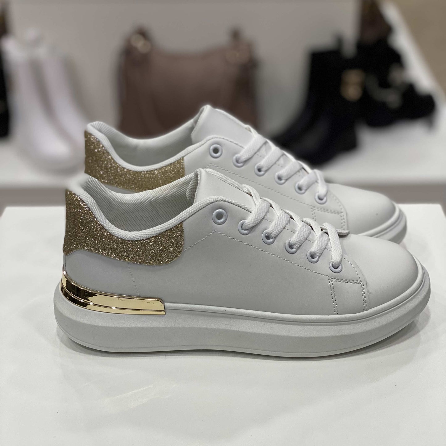 Sneakers bianche con dettaglio glitter oro sul tallone e rifiniture dorate, vista laterale su sfondo neutro