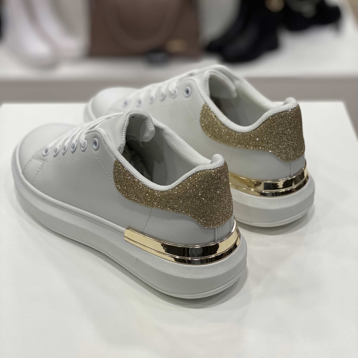 Parte posteriore di sneakers bianche con tallone glitterato oro e rifiniture dorate, vista su sfondo neutro