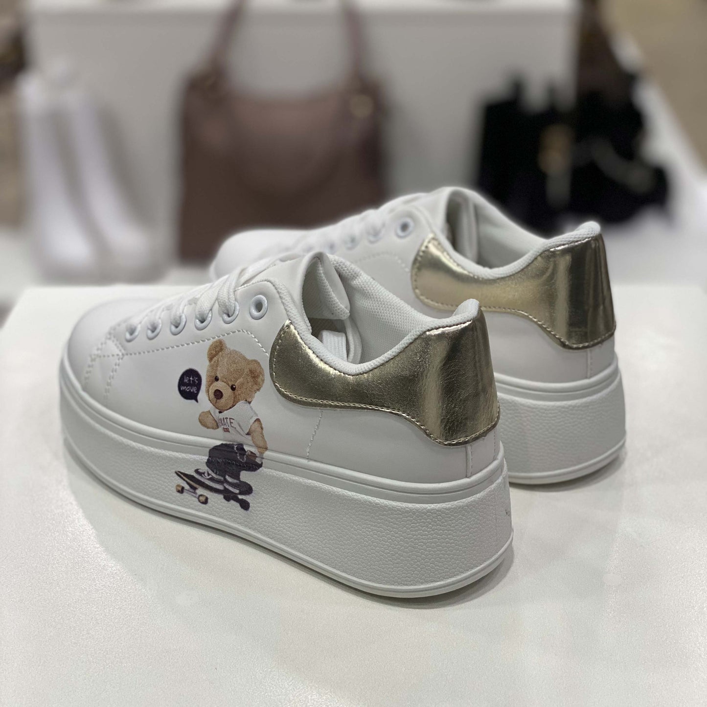 Parte posteriore di sneakers bianche con dettaglio oro sul tallone, vista del tallone su sfondo neutro