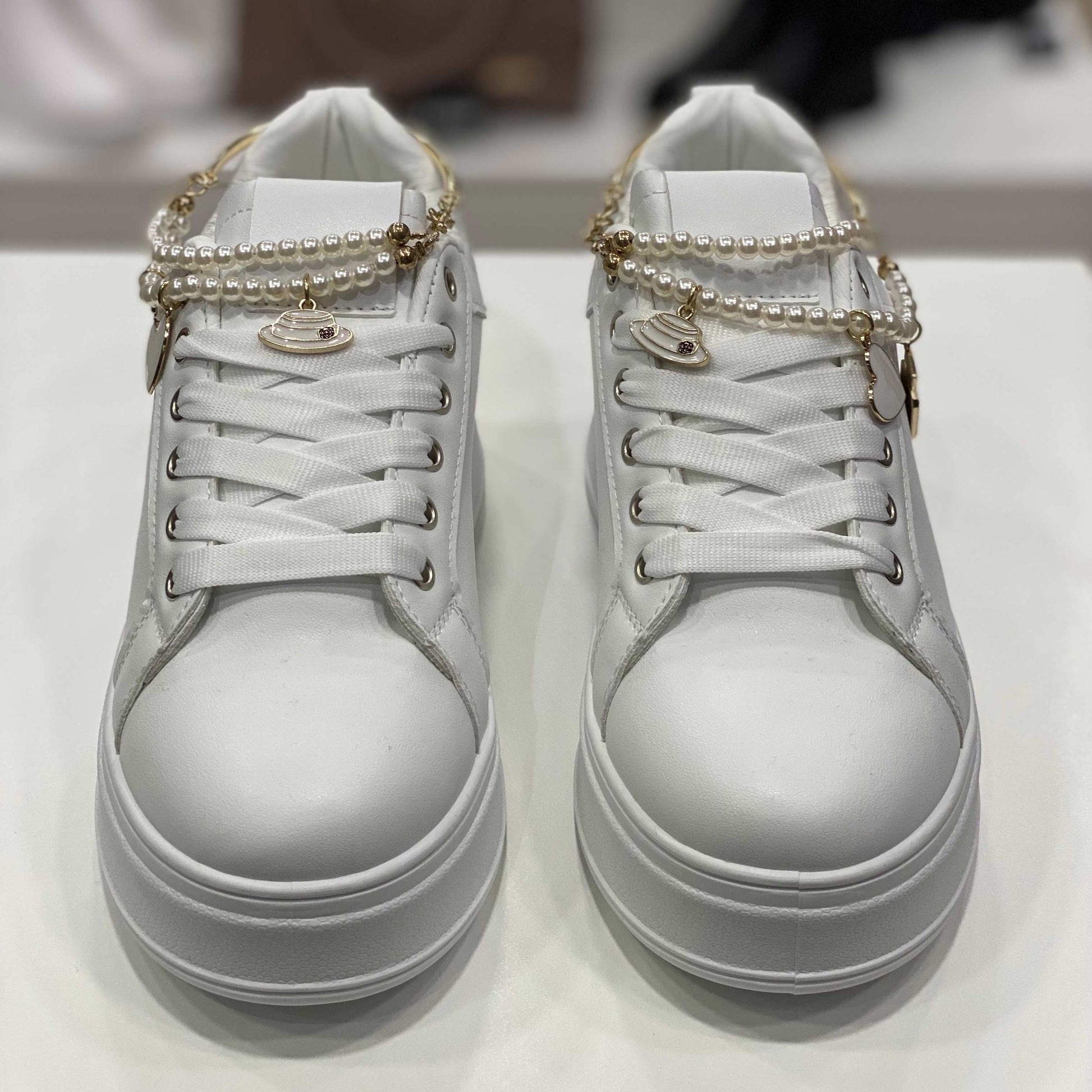 Sneakers bianche con decorazioni di perle sui lacci e dettagli dorati, vista frontale per evidenziare lo stile elegante