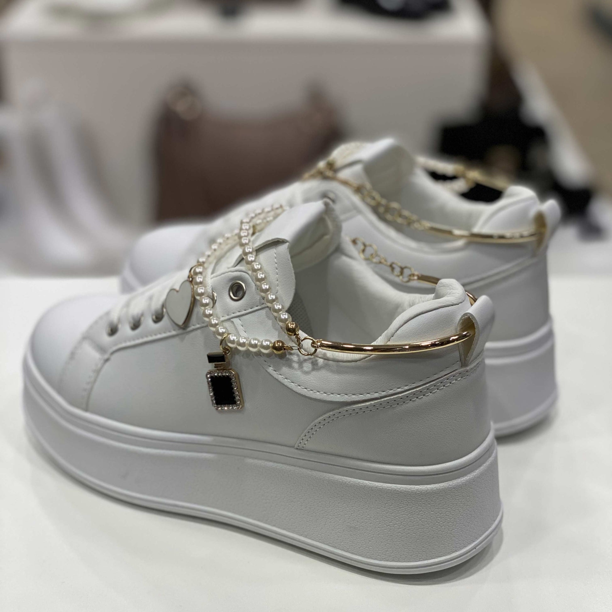 Parte posteriore di sneakers bianche con decorazioni di perle e tallone rifinito in dettagli dorati, vista del tallone su sfondo neutro