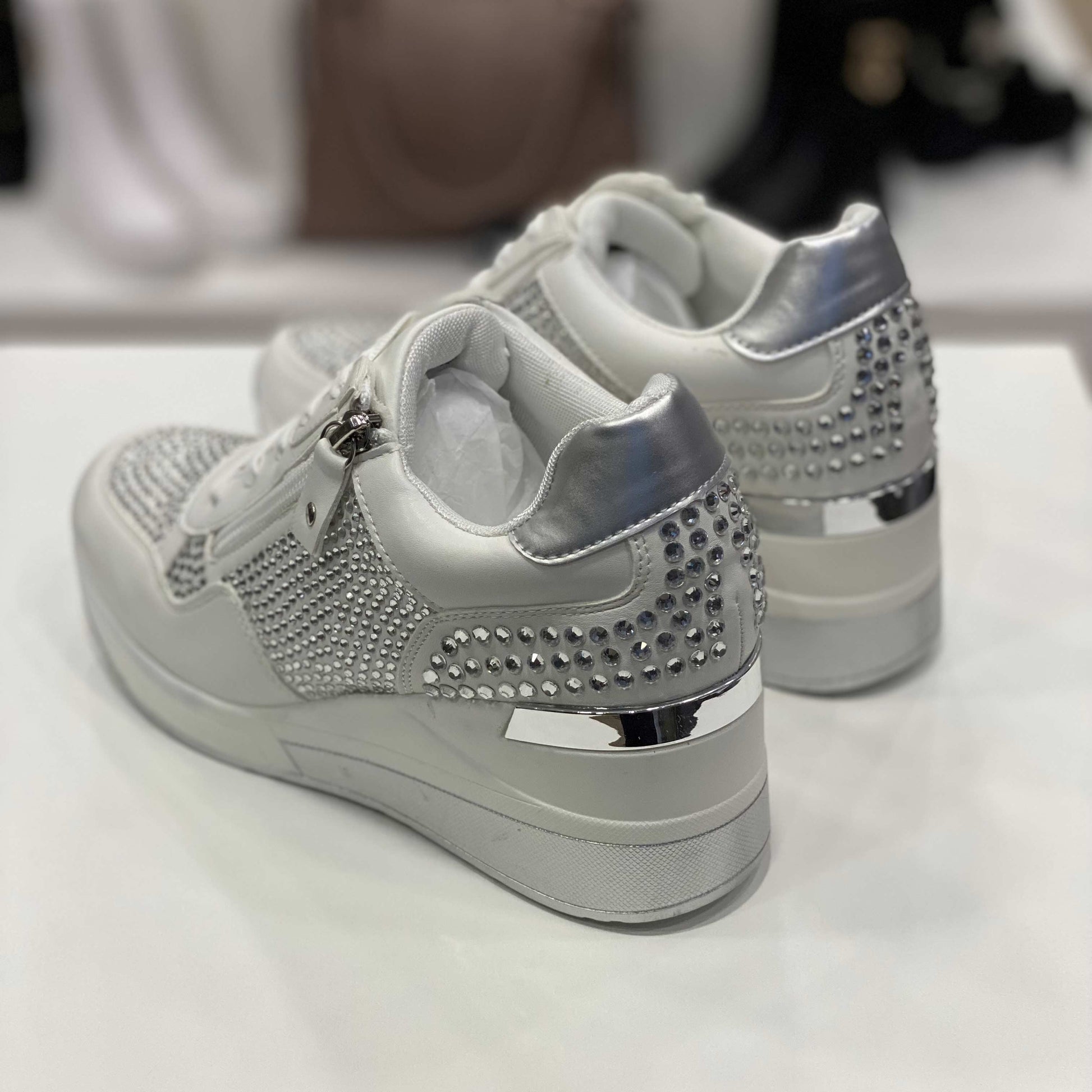 Parte posteriore di sneakers bianche con dettagli argentati e strass, vista del tallone su sfondo neutro