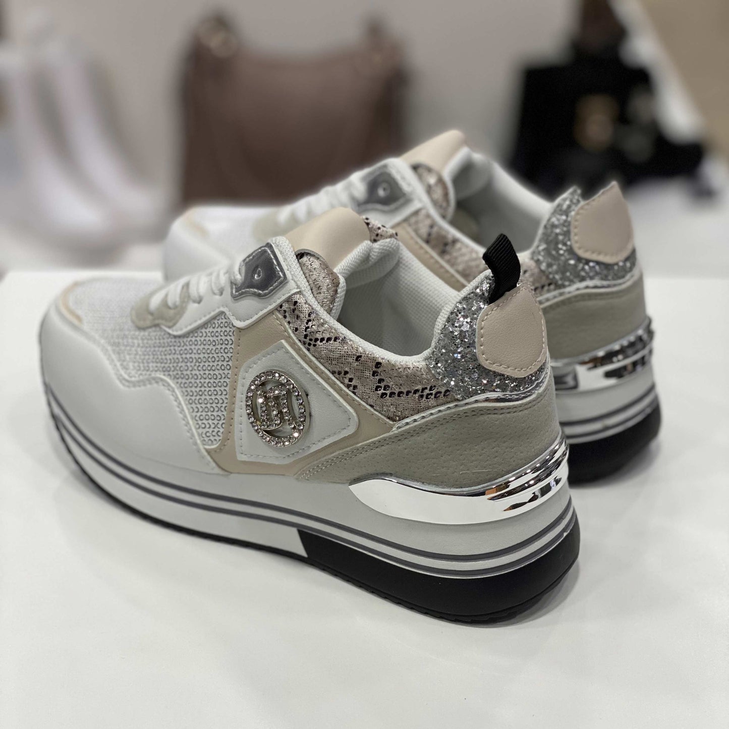 Parte posteriore di sneakers bianche con glitter argentati e tallone snake, vista su sfondo neutro