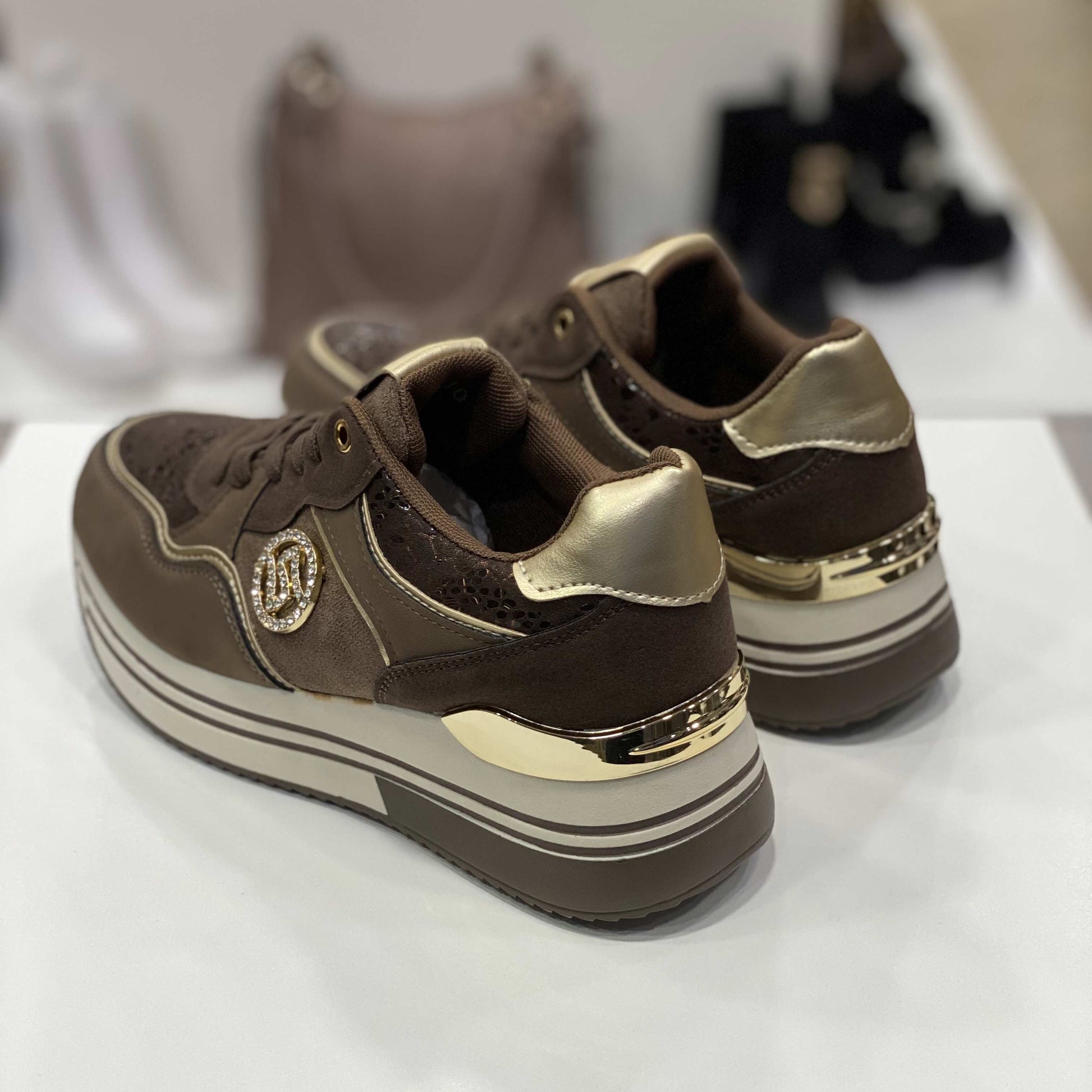 Parte posteriore di sneakers marroni con dettagli dorati e strass, vista del tallone su sfondo neutro