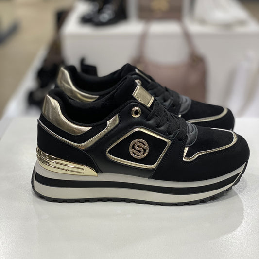 Sneakers nera con dettagli metallici dorati, vista laterale su sfondo neutro