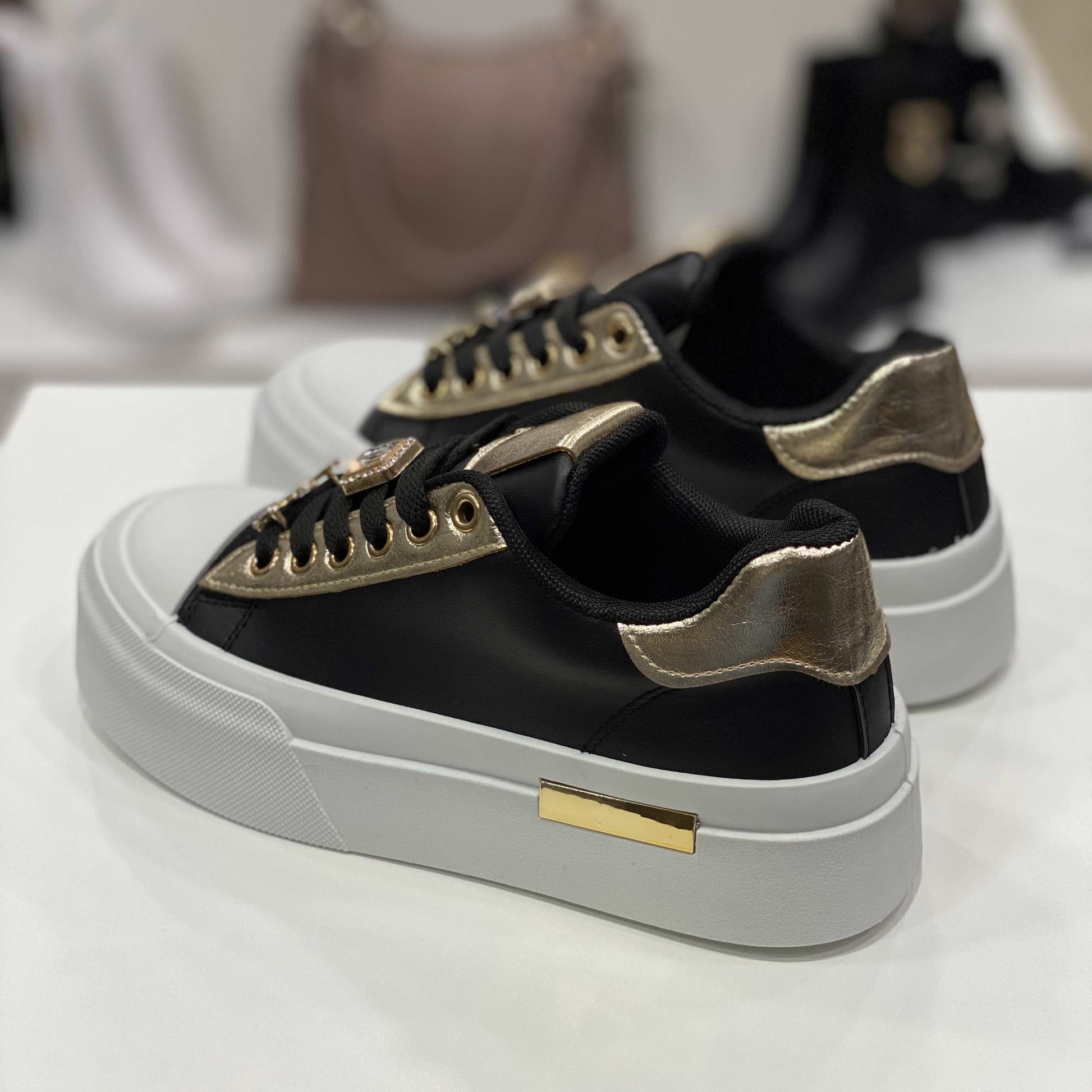Parte posteriore di sneakers nera con tallone dorato lucido e suola alta bianca, vista del tallone su sfondo neutro