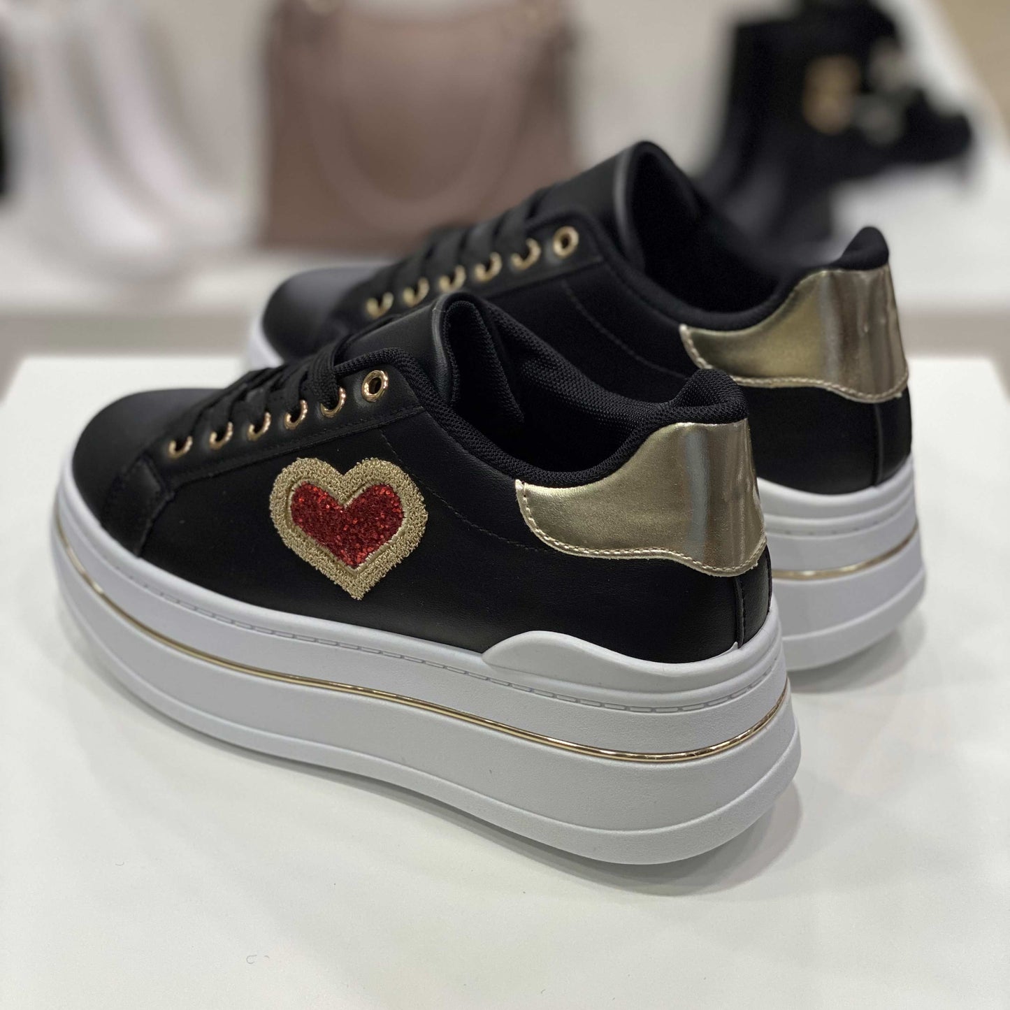 Parte posteriore di sneakers nere con tallone dorato e suola alta bianca, vista del tallone su sfondo neutro
