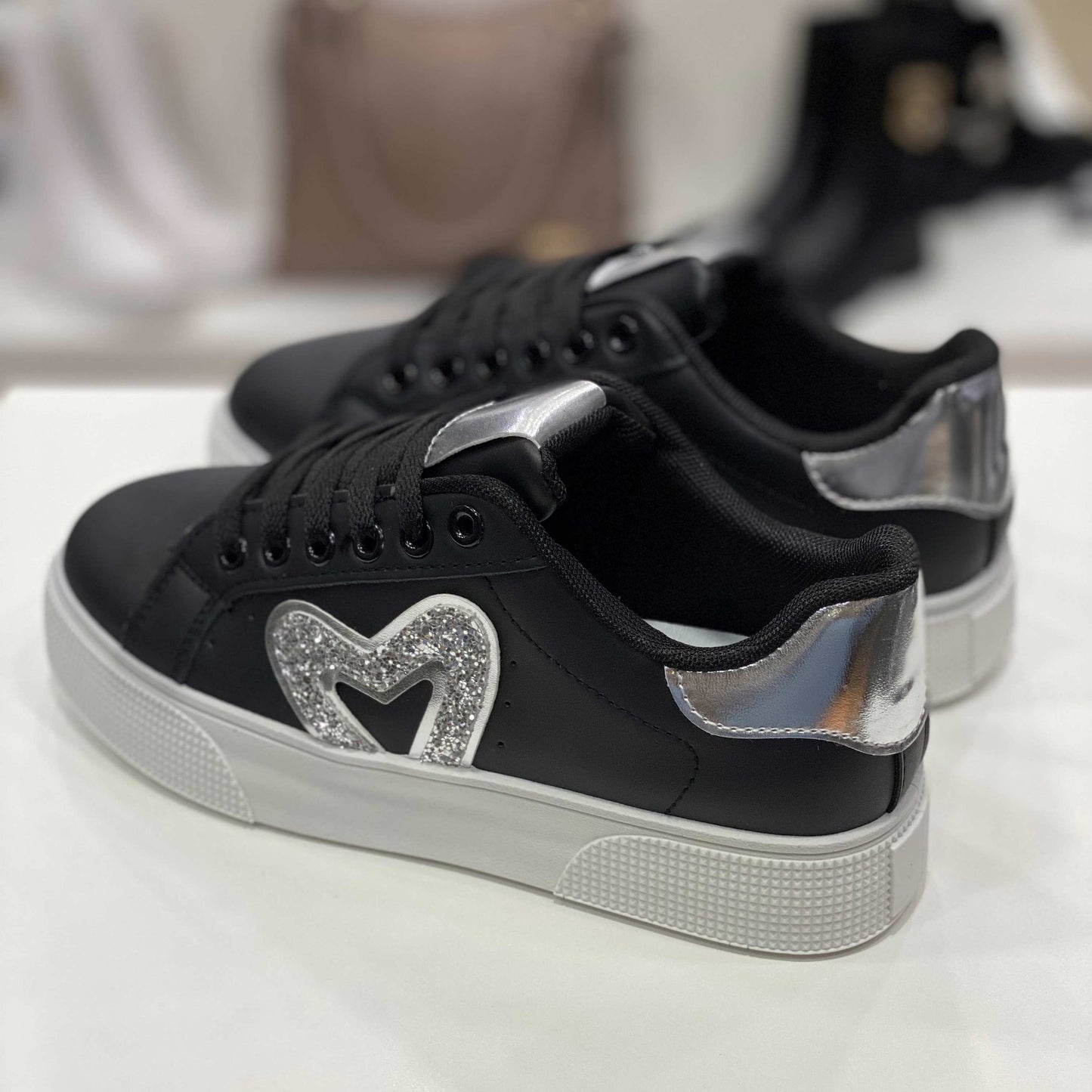 Parte posteriore di sneakers nere con tallone argento lucido e suola alta, vista del tallone su sfondo neutro