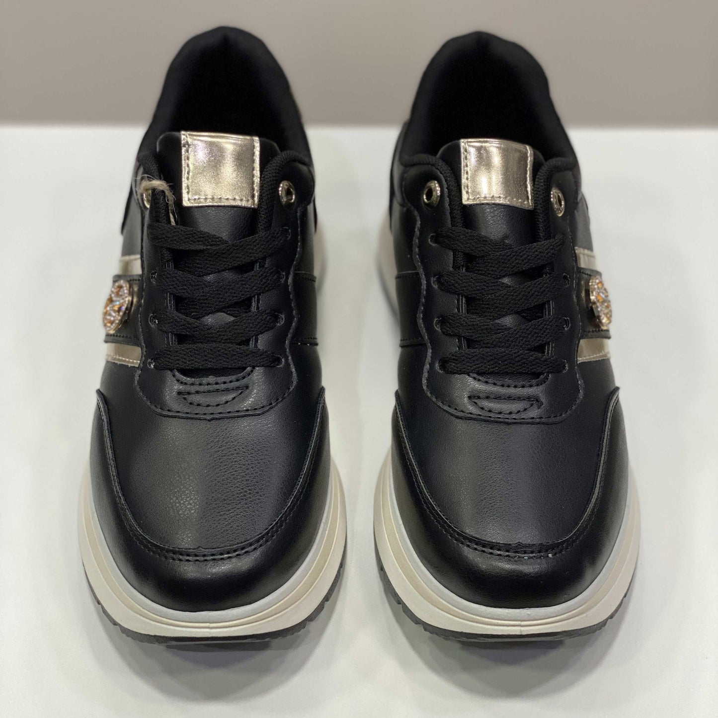 Sneakers nere con rifiniture dorate e suola bicolore, vista frontale su sfondo neutro