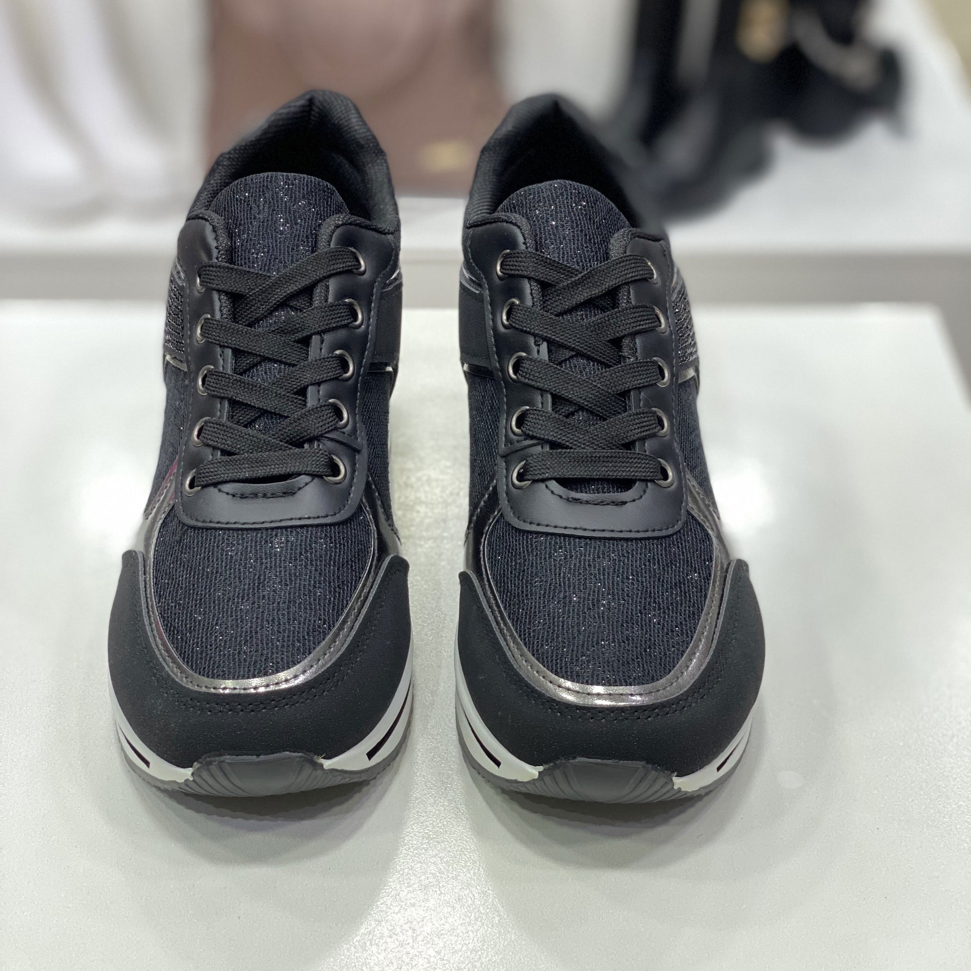 Sneakers nere con dettagli metallici argentati, vista frontale su sfondo neutro