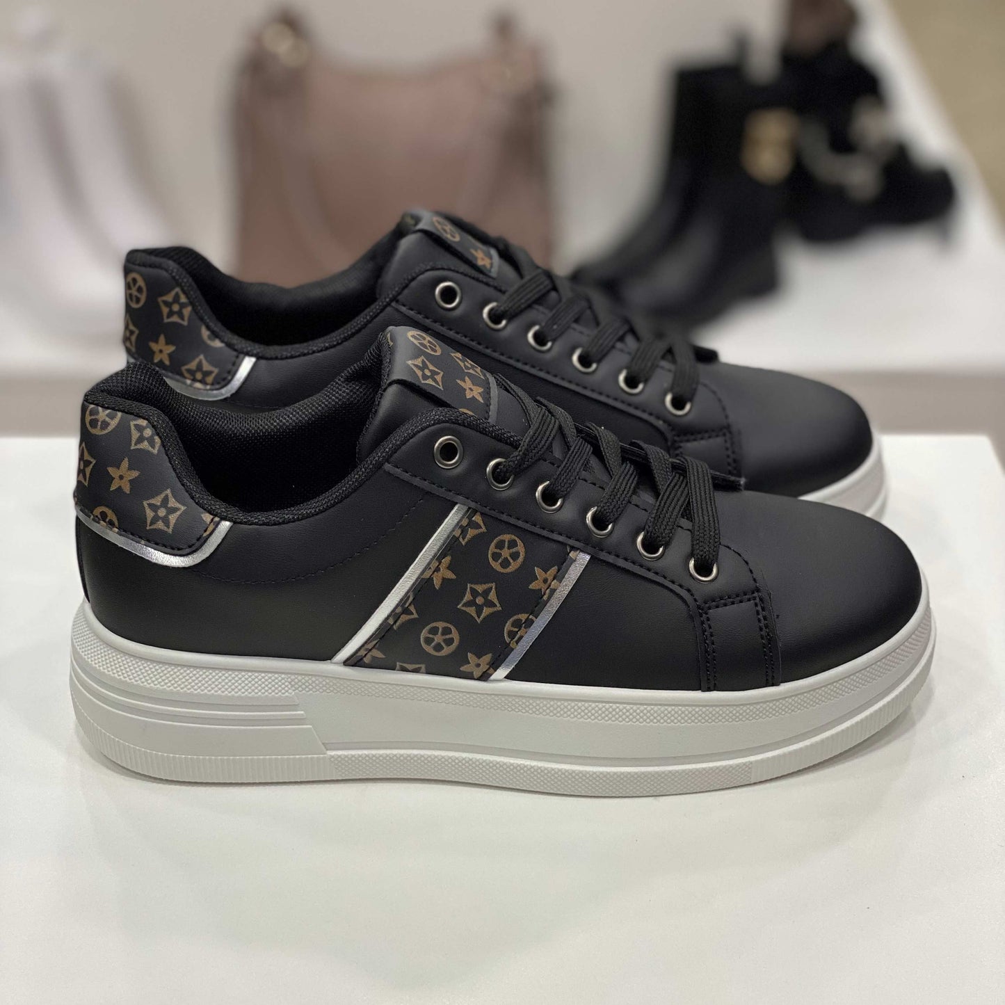 Sneakers nere con dettagli monogram marroni e suola bianca, vista laterale su sfondo neutro