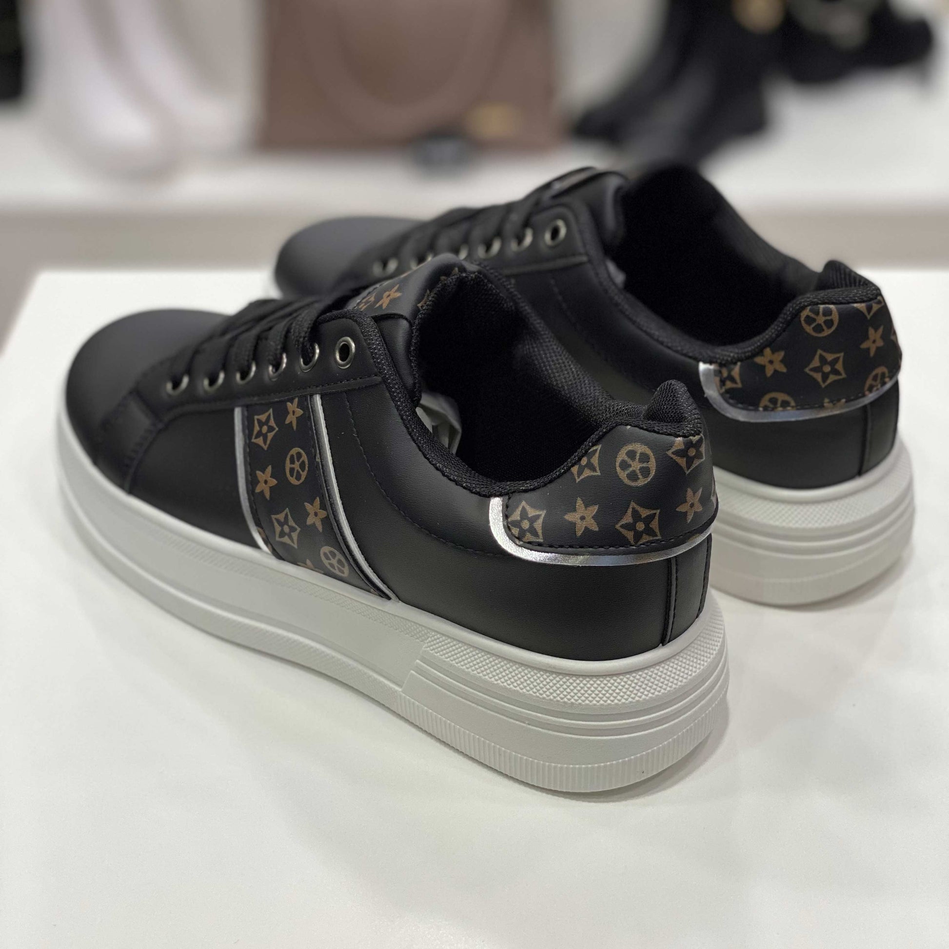 Parte posteriore di sneakers nere con dettagli monogram marroni, vista del tallone su sfondo neutro