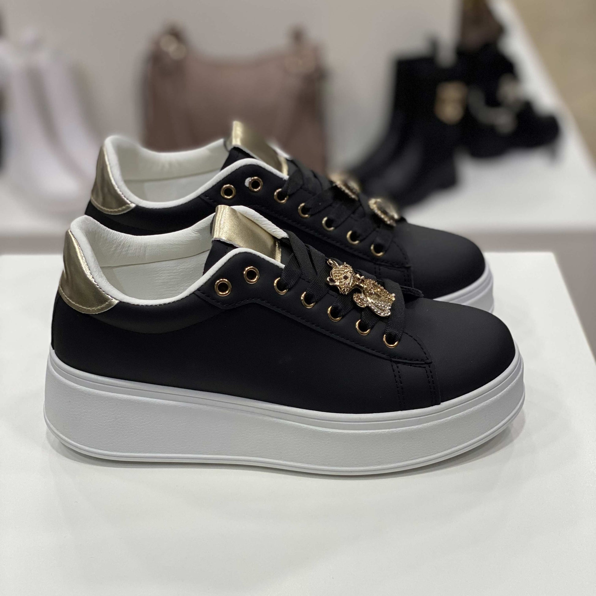 Sneakers nere con gioiello a forma di gatto e cuore, dettagli dorati sulla linguetta e tallone, vista laterale per evidenziare il design elegante