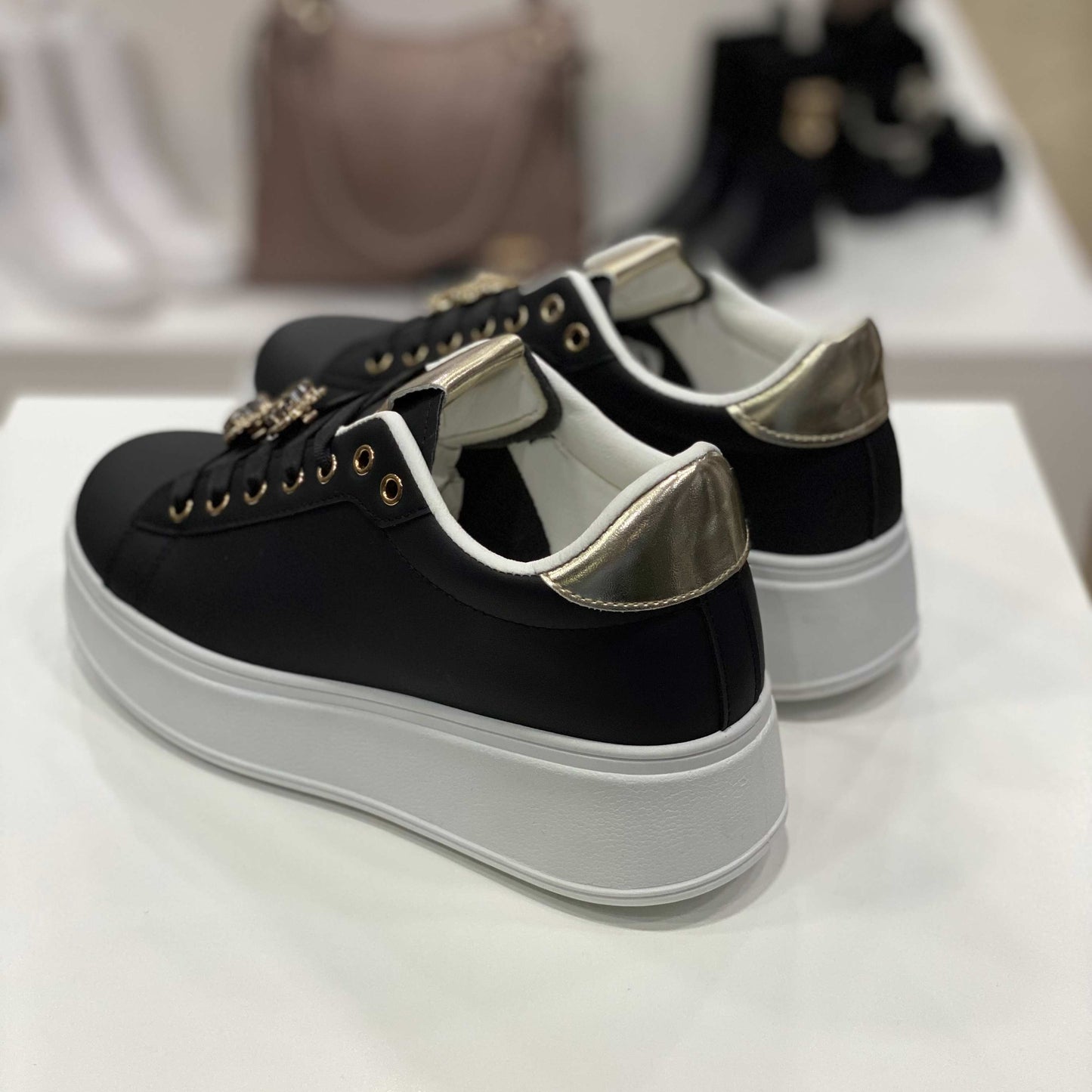 Parte posteriore di sneakers nere con dettagli dorati sul tallone, vista su sfondo neutro