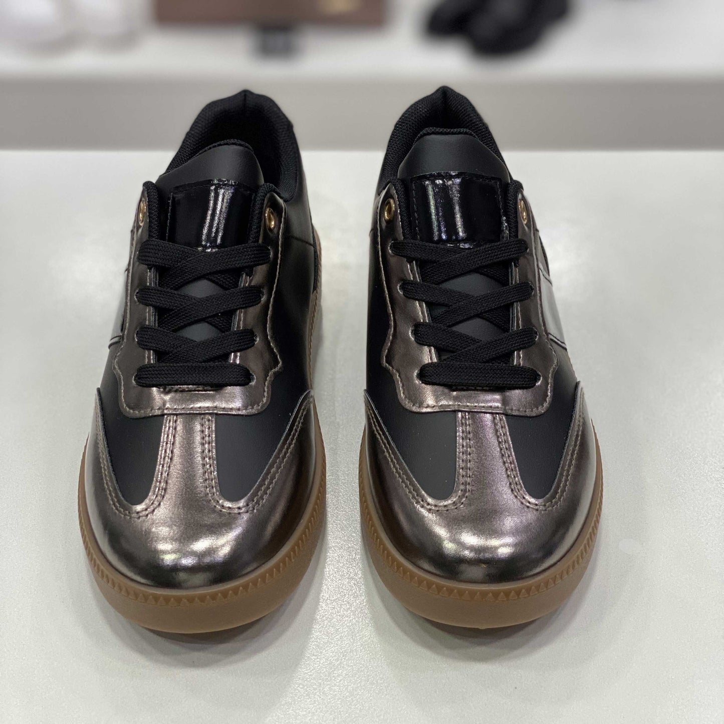 Sneakers nere con dettagli metallizzati color bronzo e suola in gomma, vista frontale su sfondo neutro