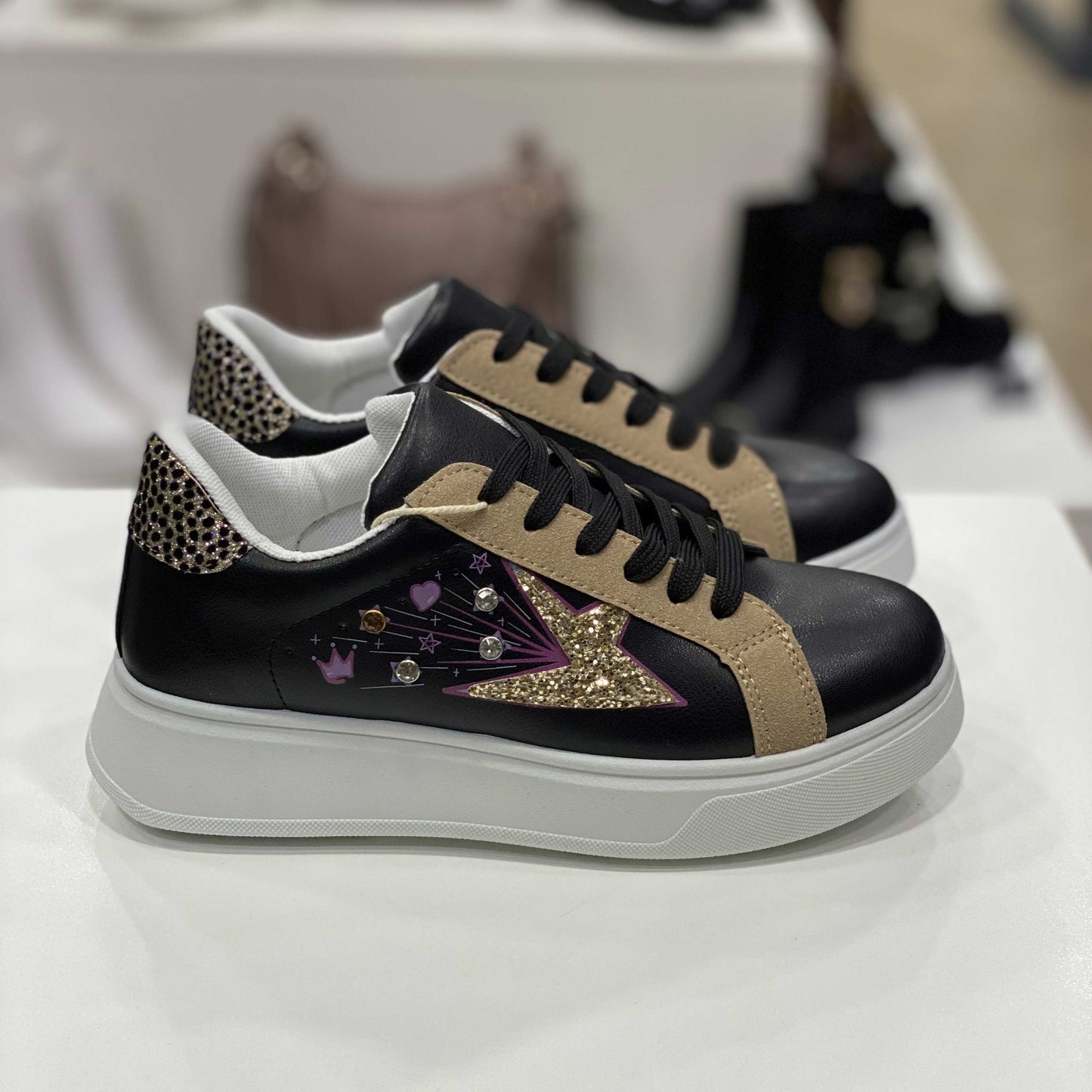 Sneakers nere con stella glitterata dorata, dettagli beige e decorazioni colorate, vista laterale su sfondo neutro