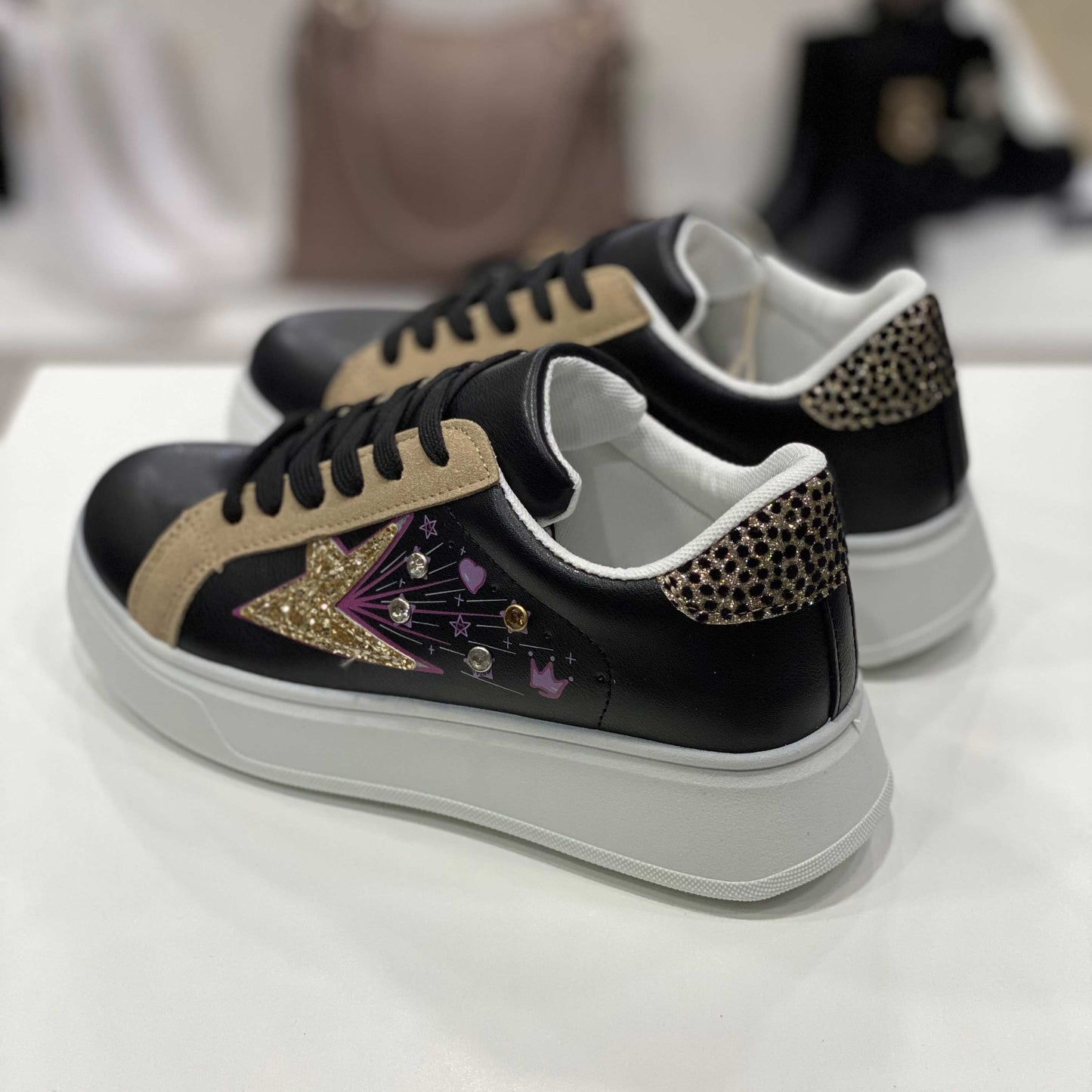 Parte posteriore di sneakers nere con tallone decorato a pois dorati e dettagli eleganti, vista del tallone su sfondo neutro