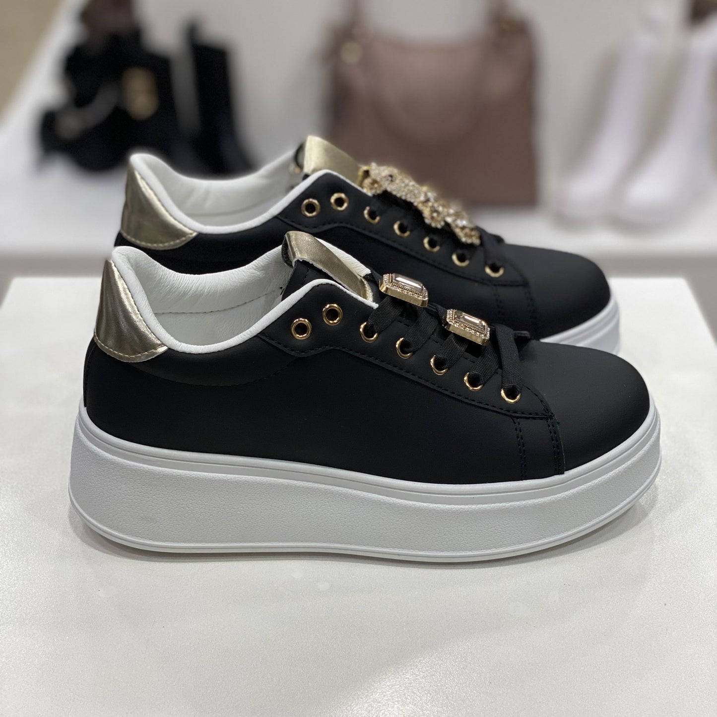 Sneakers nere con dettagli metallici dorati e suola platform bianca, vista laterale.